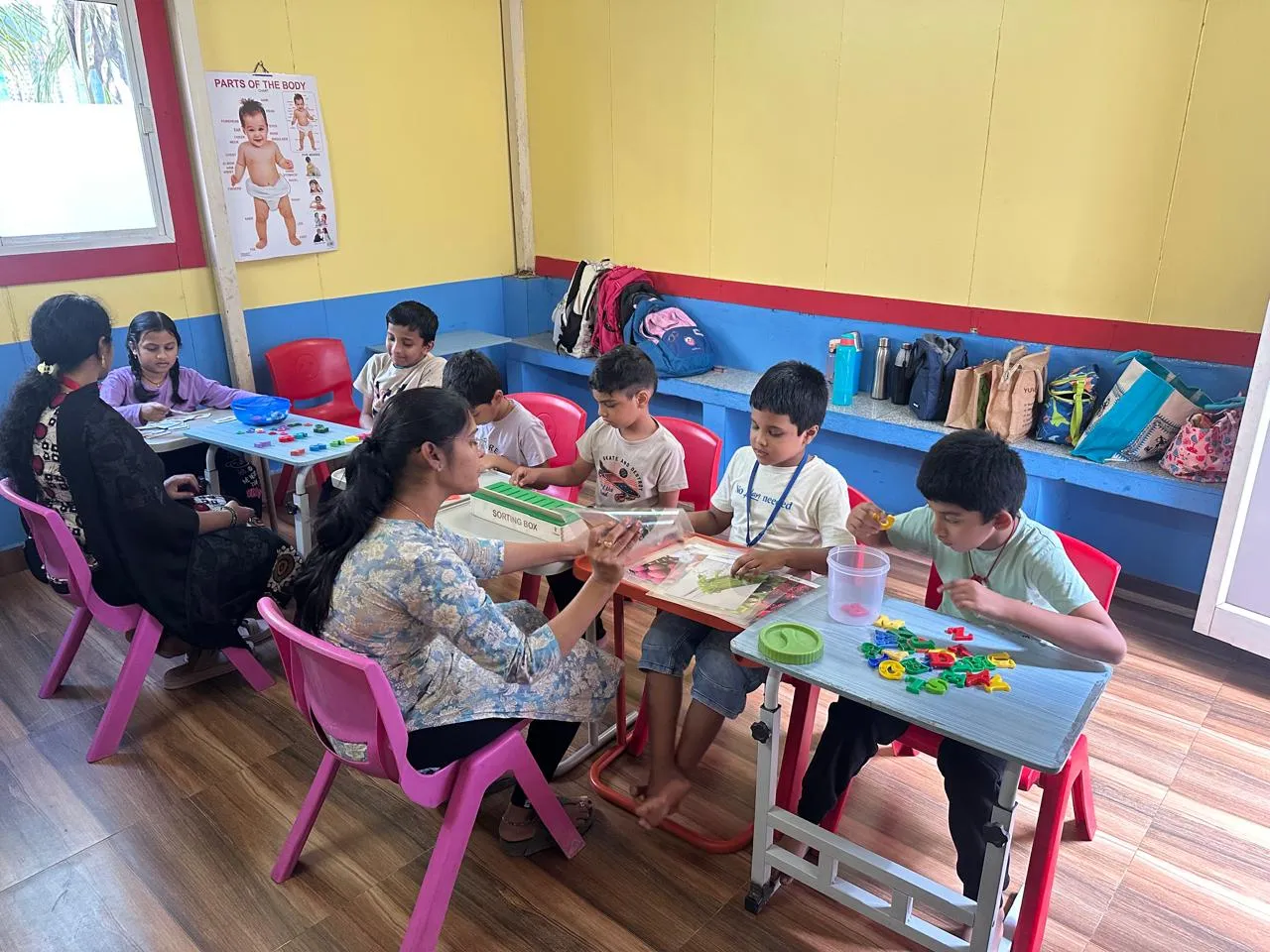 Teachers working with children at their desks using letters, sorting boxes and picture cards