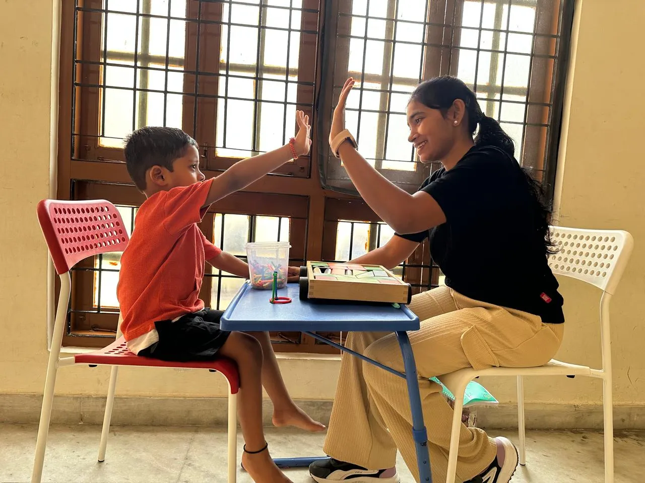 A boy and his teacher sharing a high five during a table activity