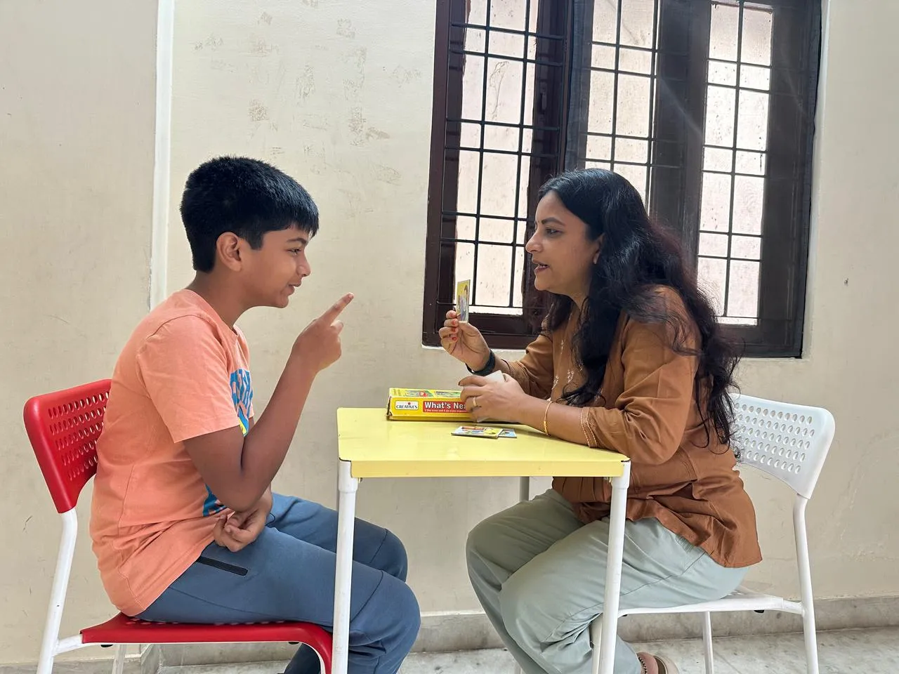 A teacher and a boy talking face to face across a table, using picture cards
