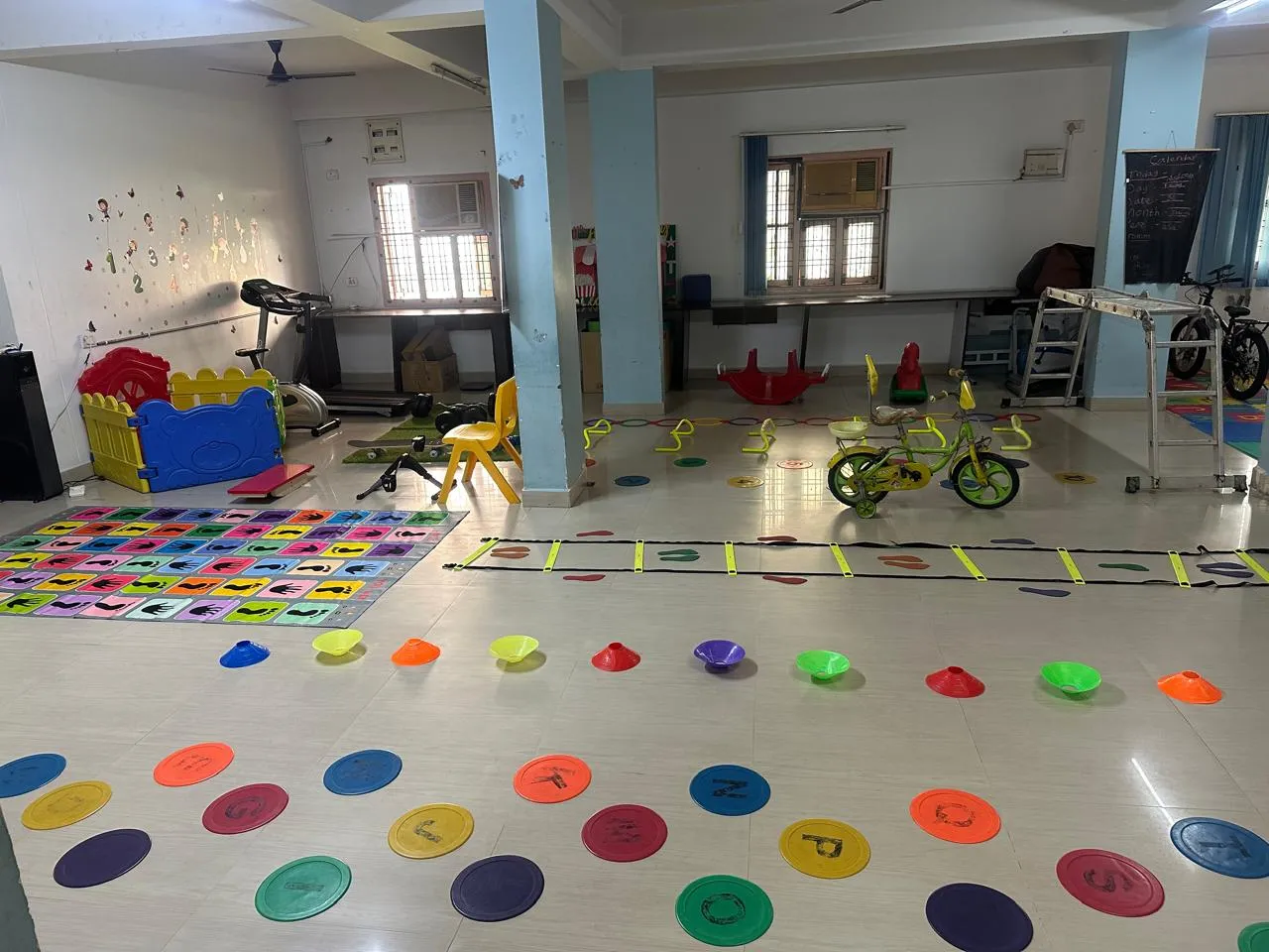 The activity room set up with floor spots, cones, an agility ladder, a balance board and a bicycle